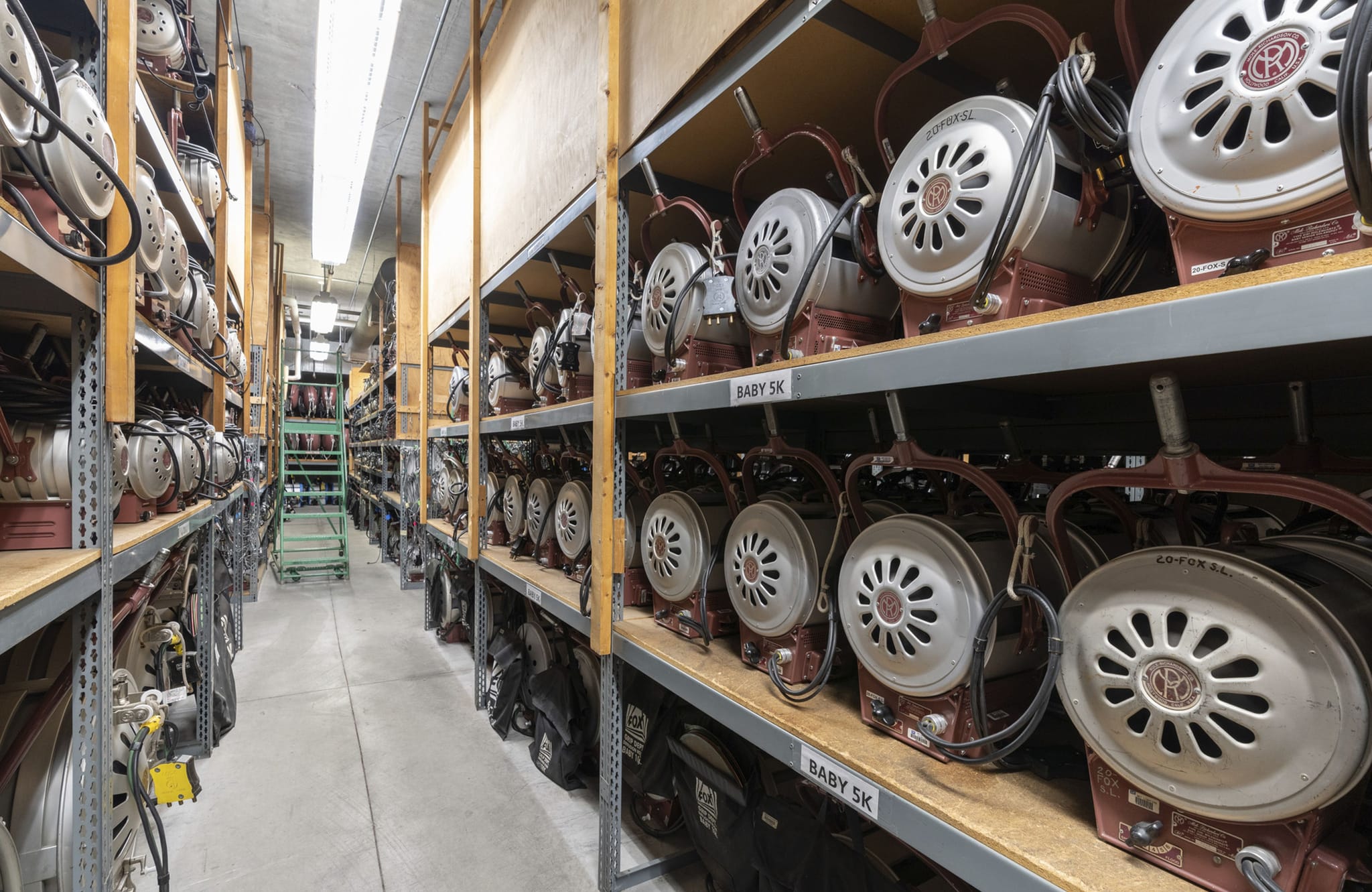 Rows of shelves filled with vintage film and stage lights in a long storage room.