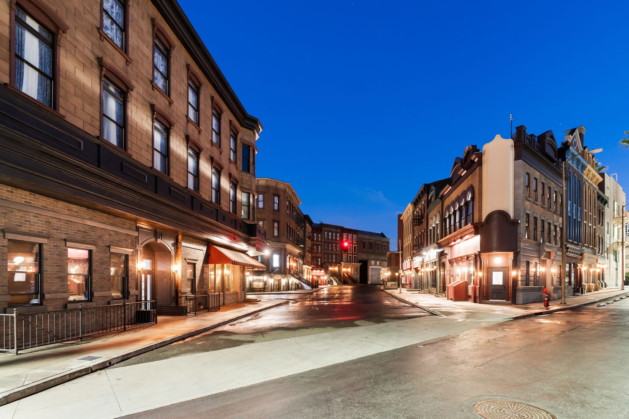 A deserted city street corner at night, with historic buildings, illuminated shops, and wet pavement reflecting the lights.