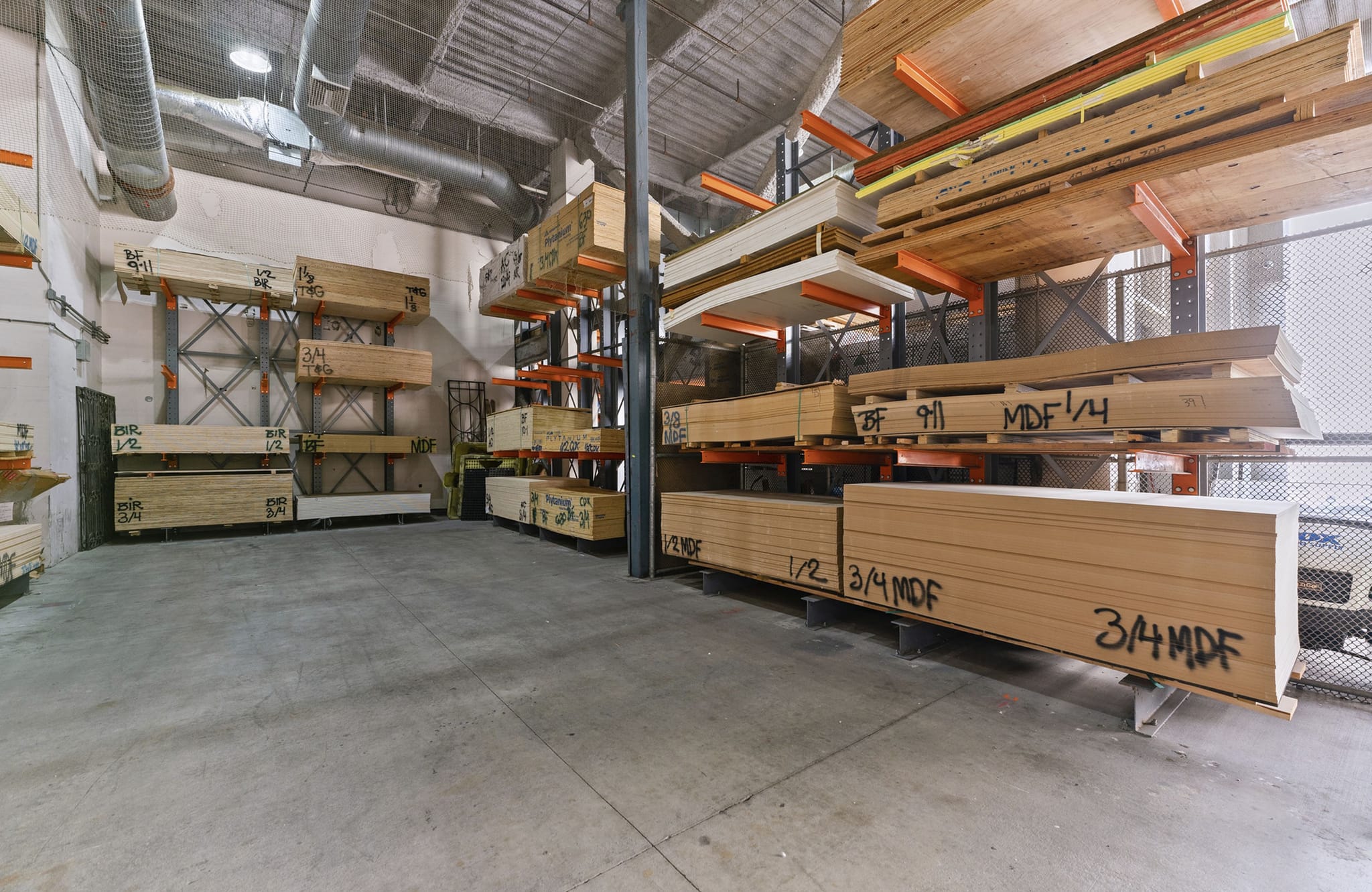 A large warehouse with stacks of various lumber and MDF panels stored on tall metal racks.