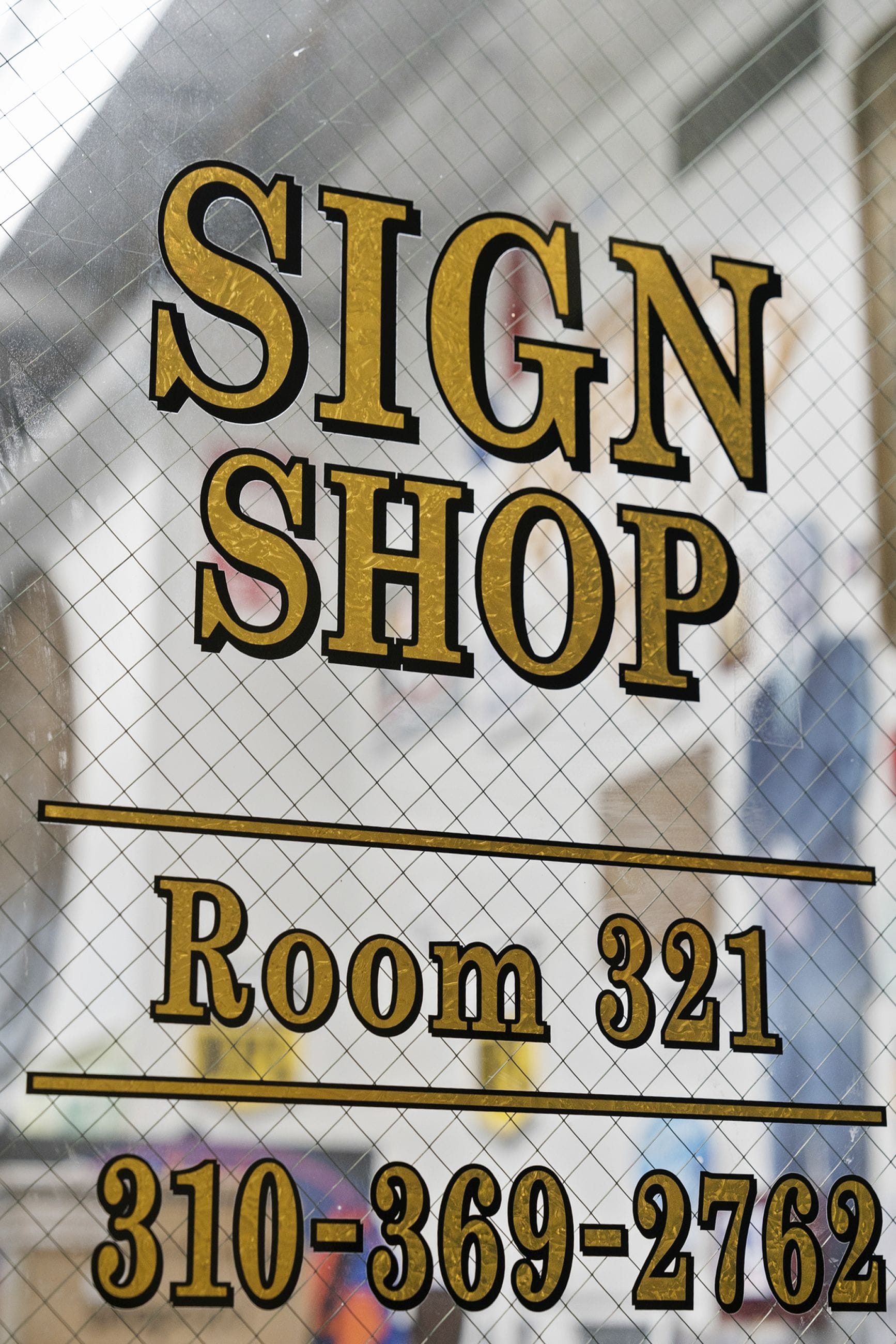 Gold text on a grid-patterned glass door reads "SIGN SHOP Room 321 310-369-2762".