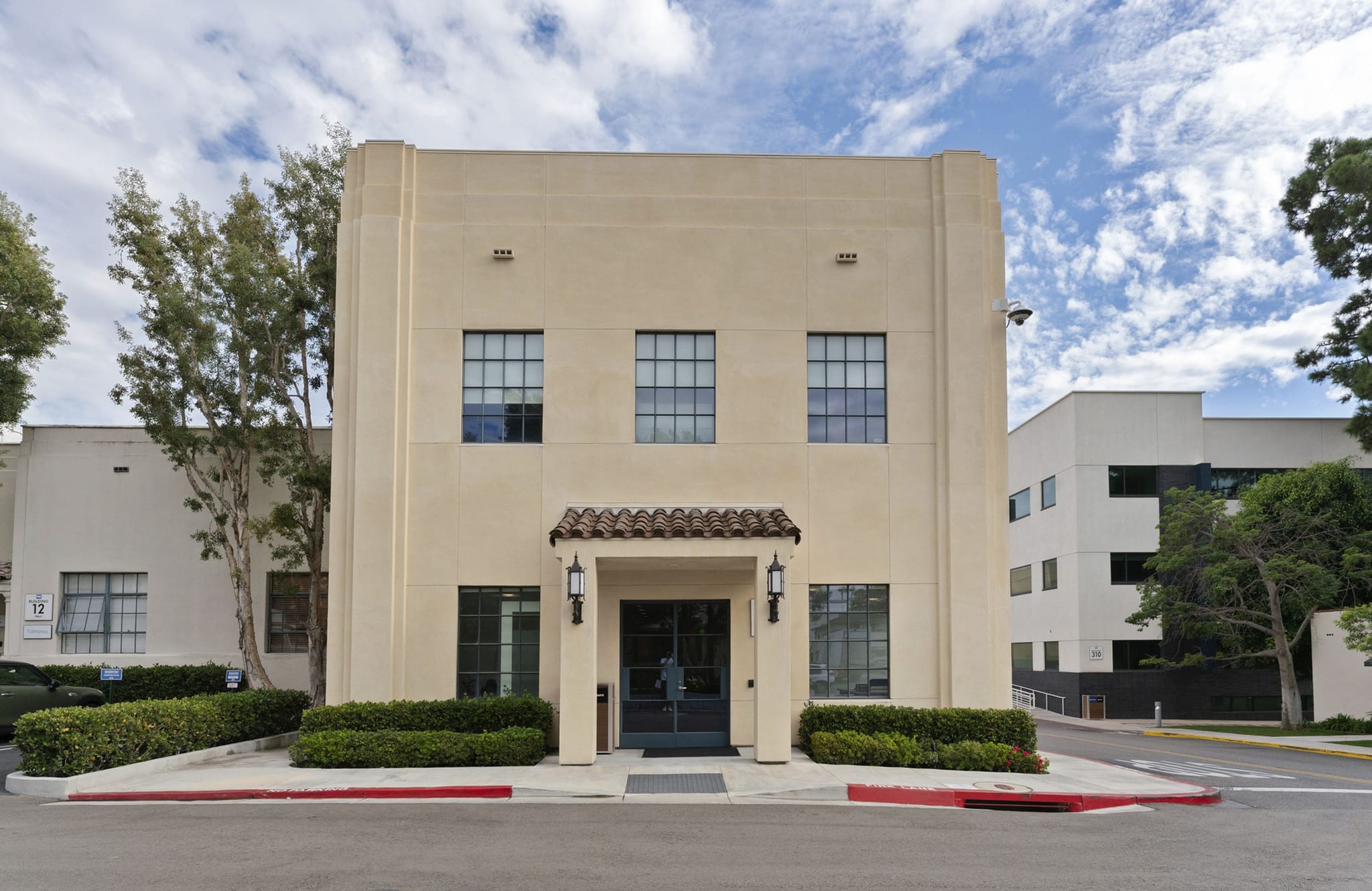 A cream-colored, two-story Art Deco building with a terracotta-tiled entrance awning.