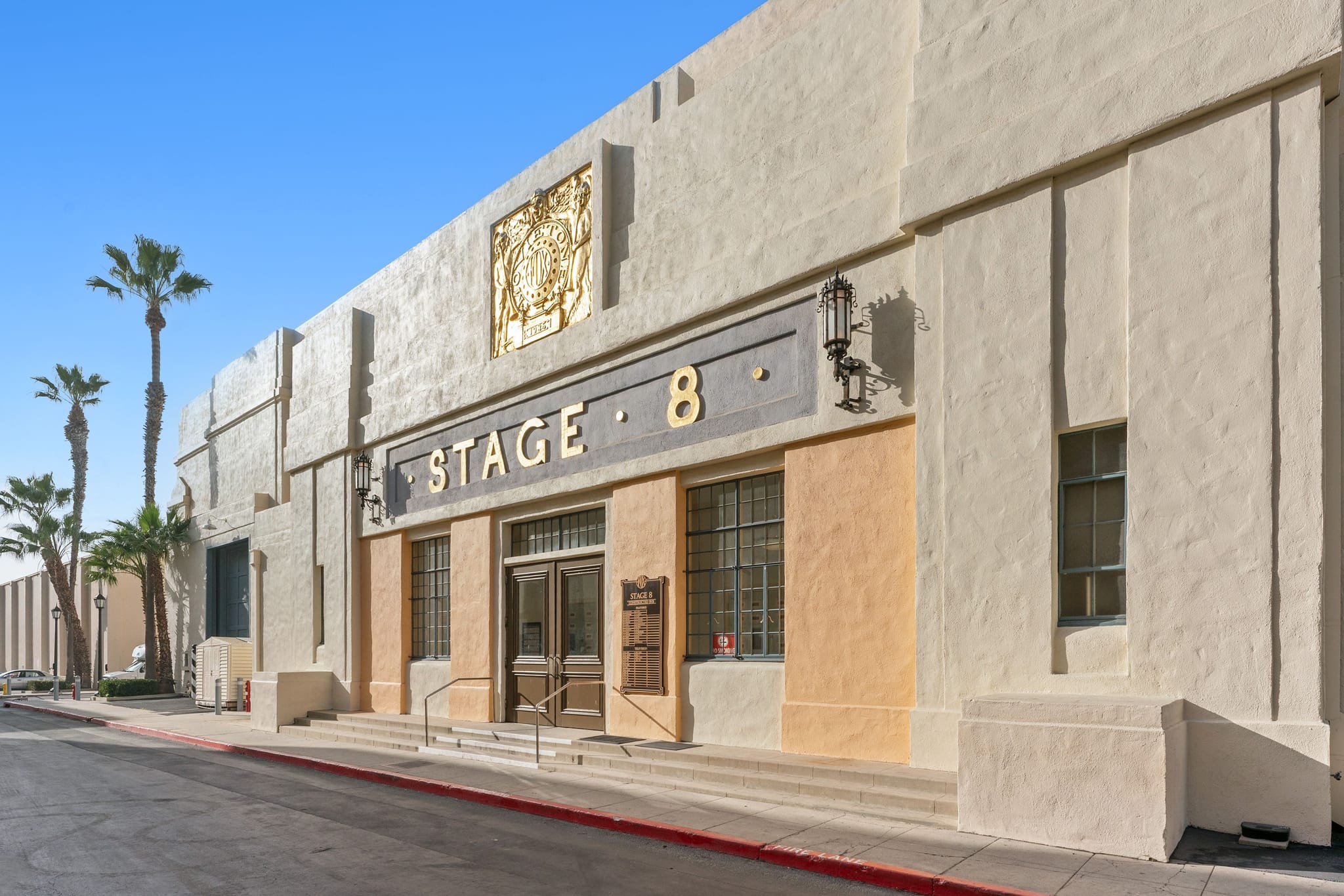 A two-story tan commercial building with Art Deco architectural features, a tiled entrance canopy, and dark-framed windows.