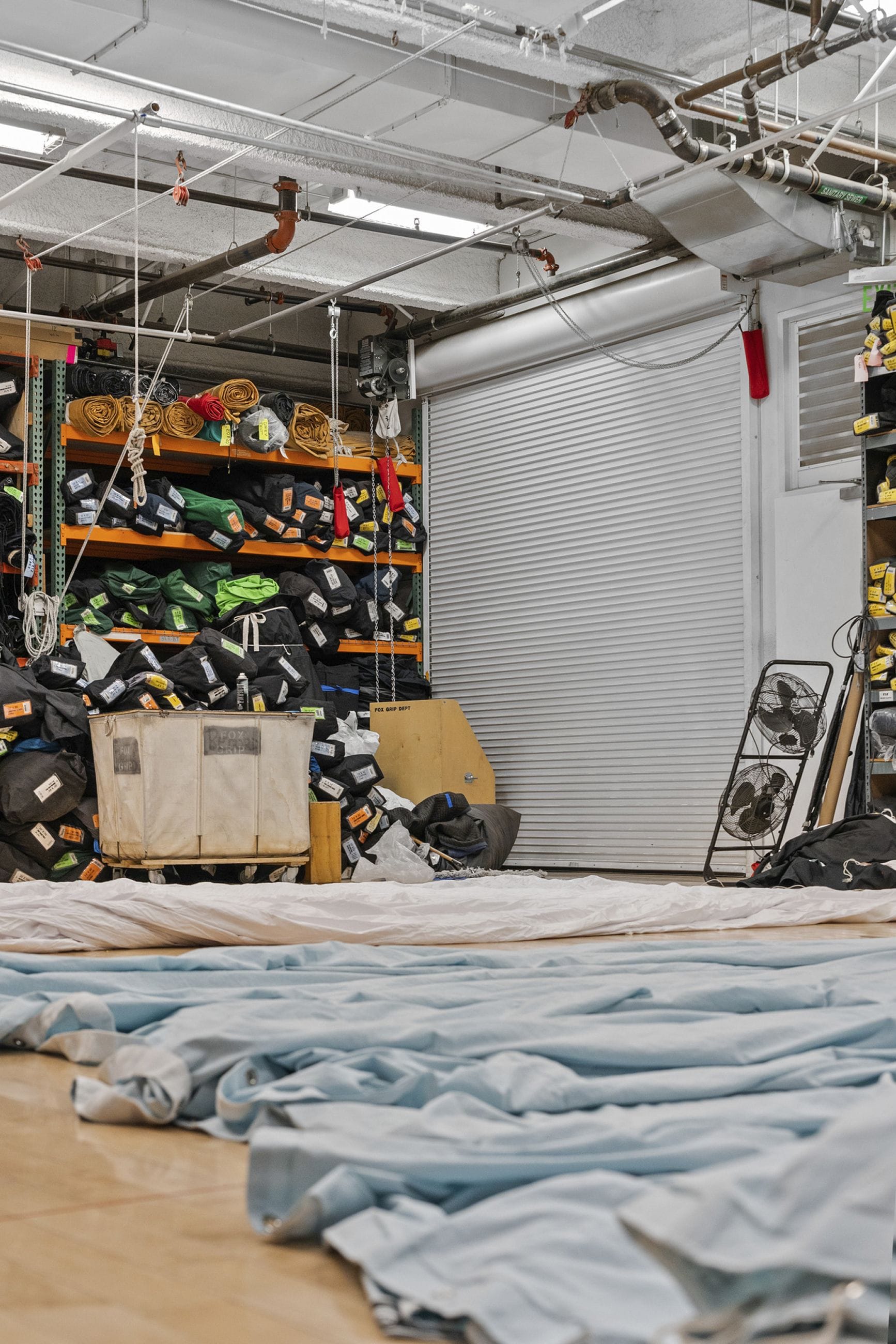 Light blue fabric spread on a floor in a warehouse with shelves of bundled gear, a roll-up door, and exposed ceiling pipes.