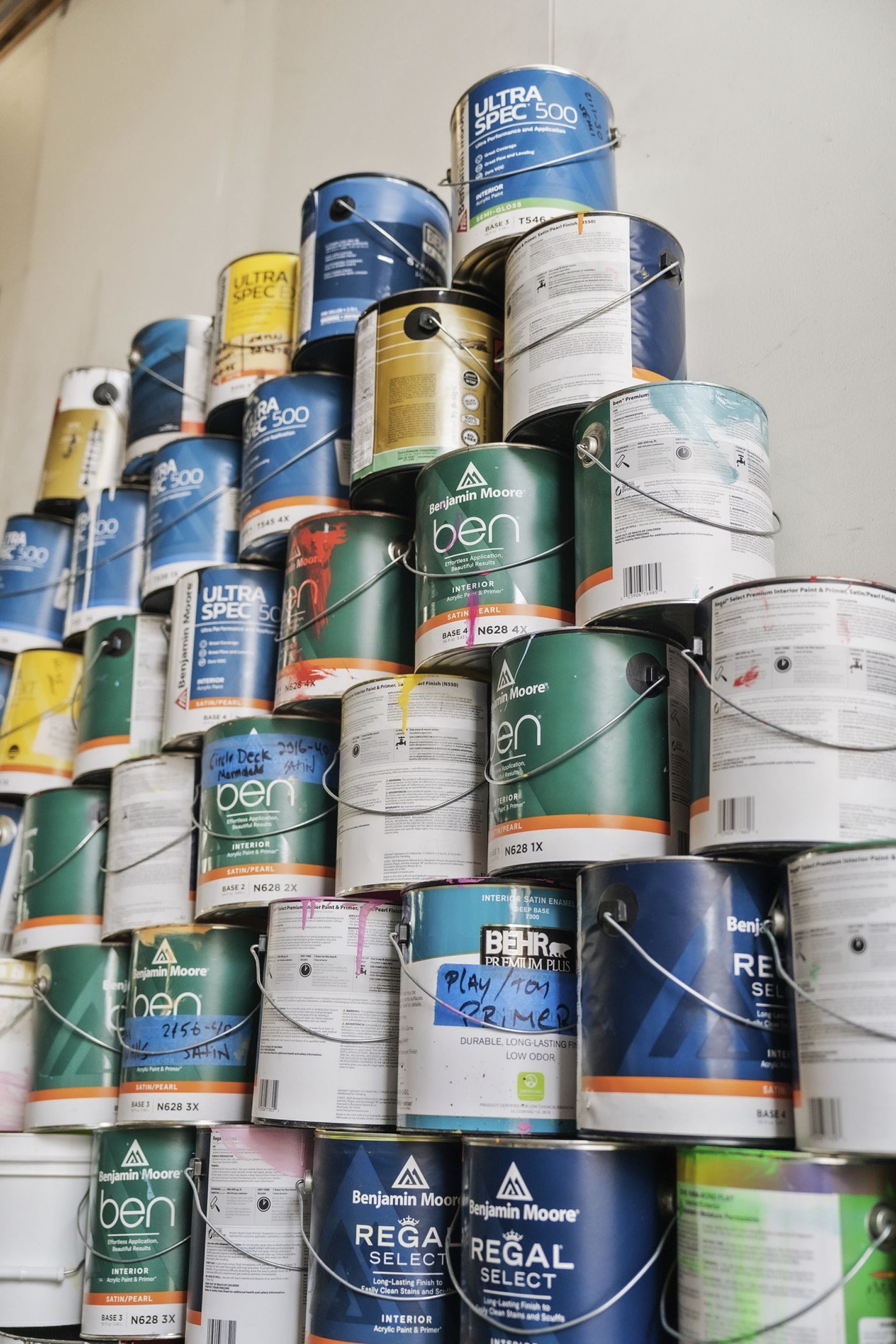 A large, messy stack of numerous paint cans from various brands like Benjamin Moore and Behr.