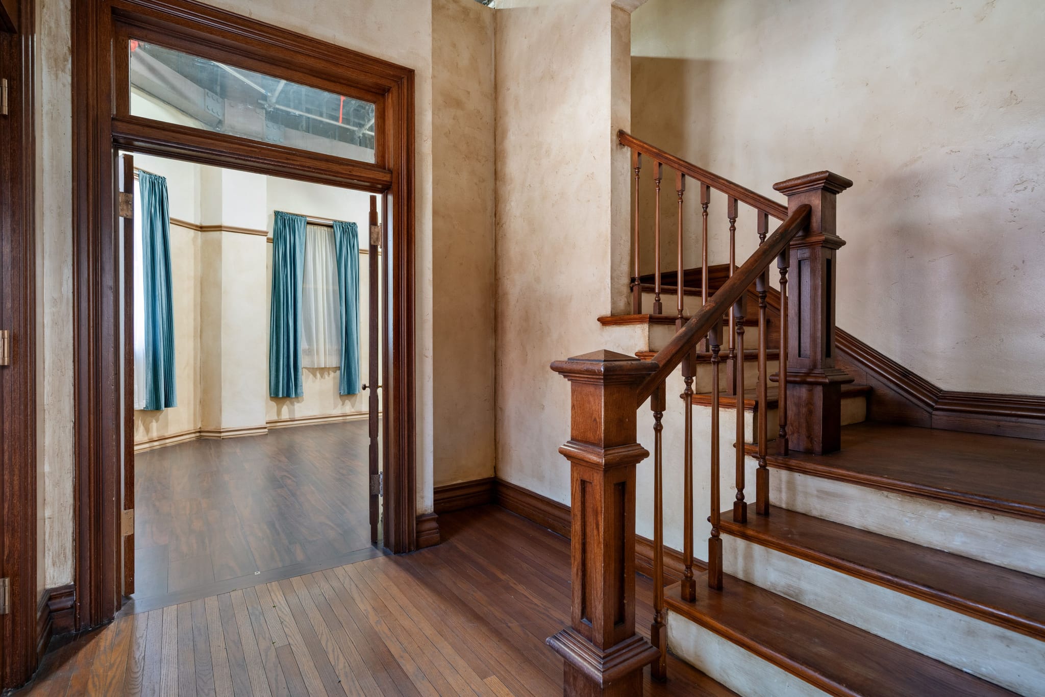 Dark wood staircase on the right of an open doorway leading to a room with blue curtains.