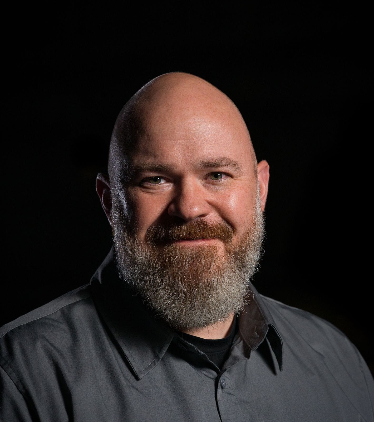 Headshot of a smiling bald man with a salt-and-pepper beard, wearing a dark grey shirt.