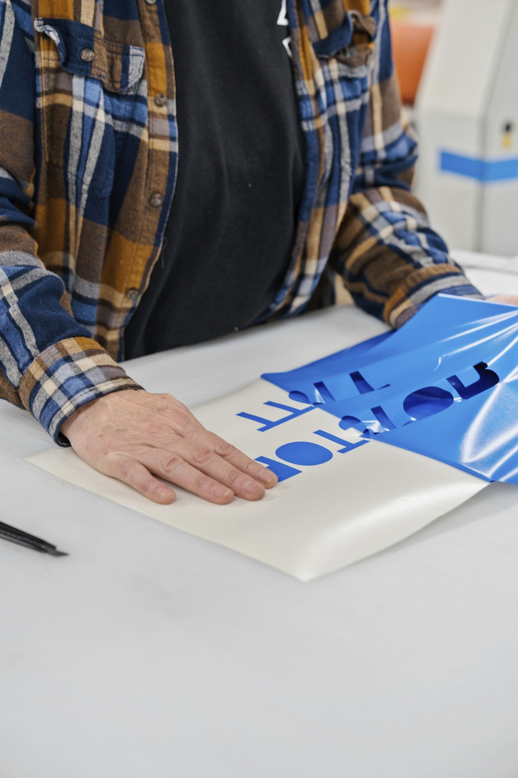 A person peels blue vinyl from a white sheet, revealing blue letters.
