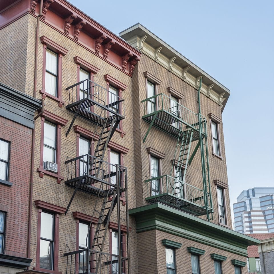 Two brick apartment buildings with black and dark green fire escapes.