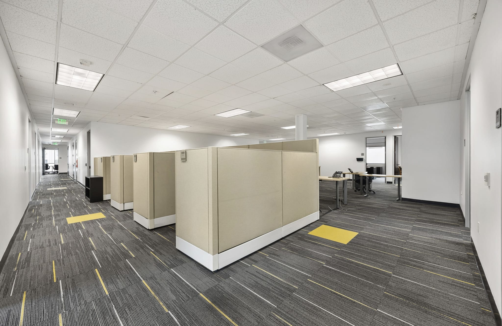 Modern office with tan cubicles, a hallway, and patterned carpet.
