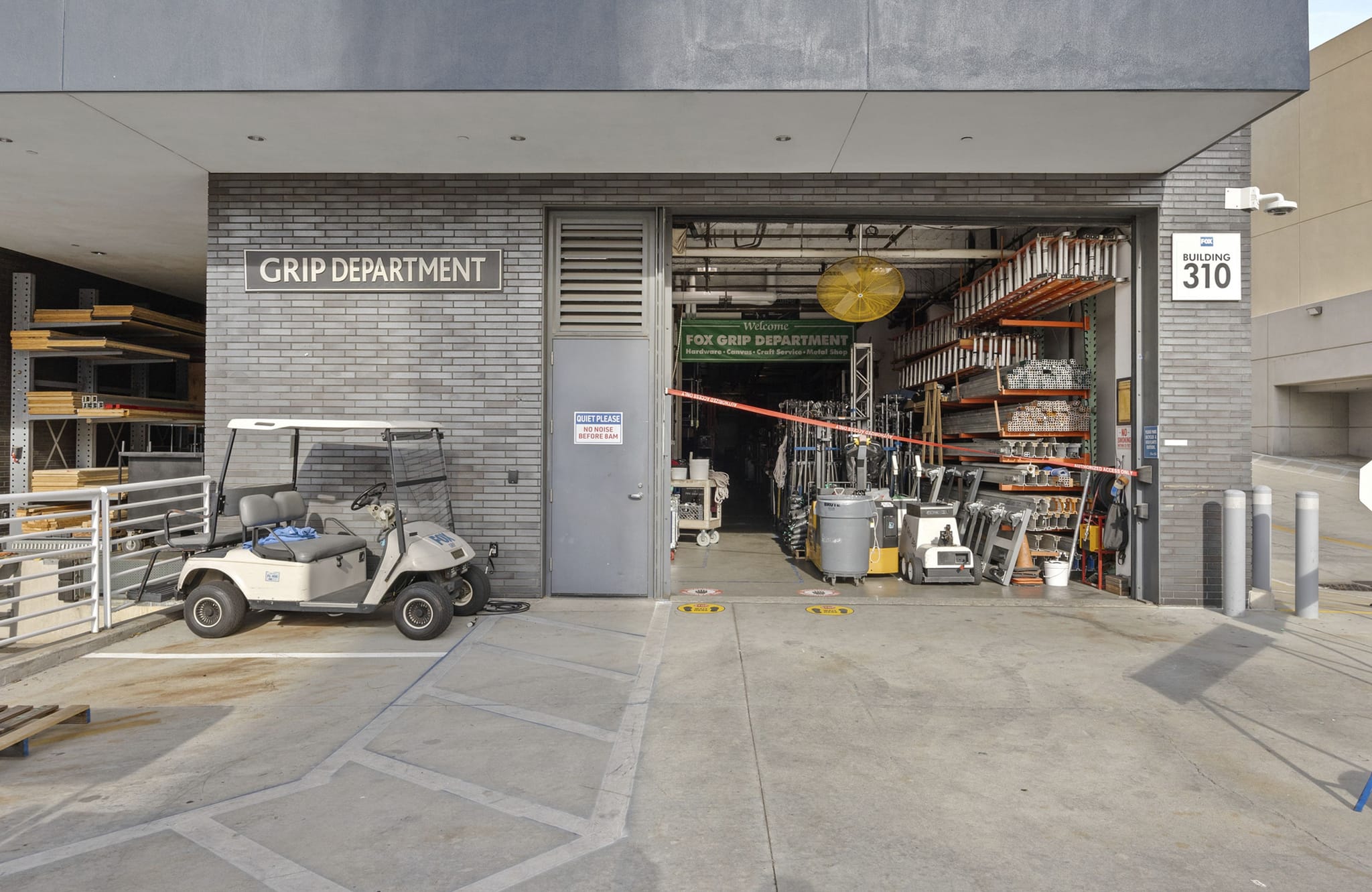 Exterior of the "Grip Department" building with an open bay door revealing film equipment, and a golf cart parked outside.