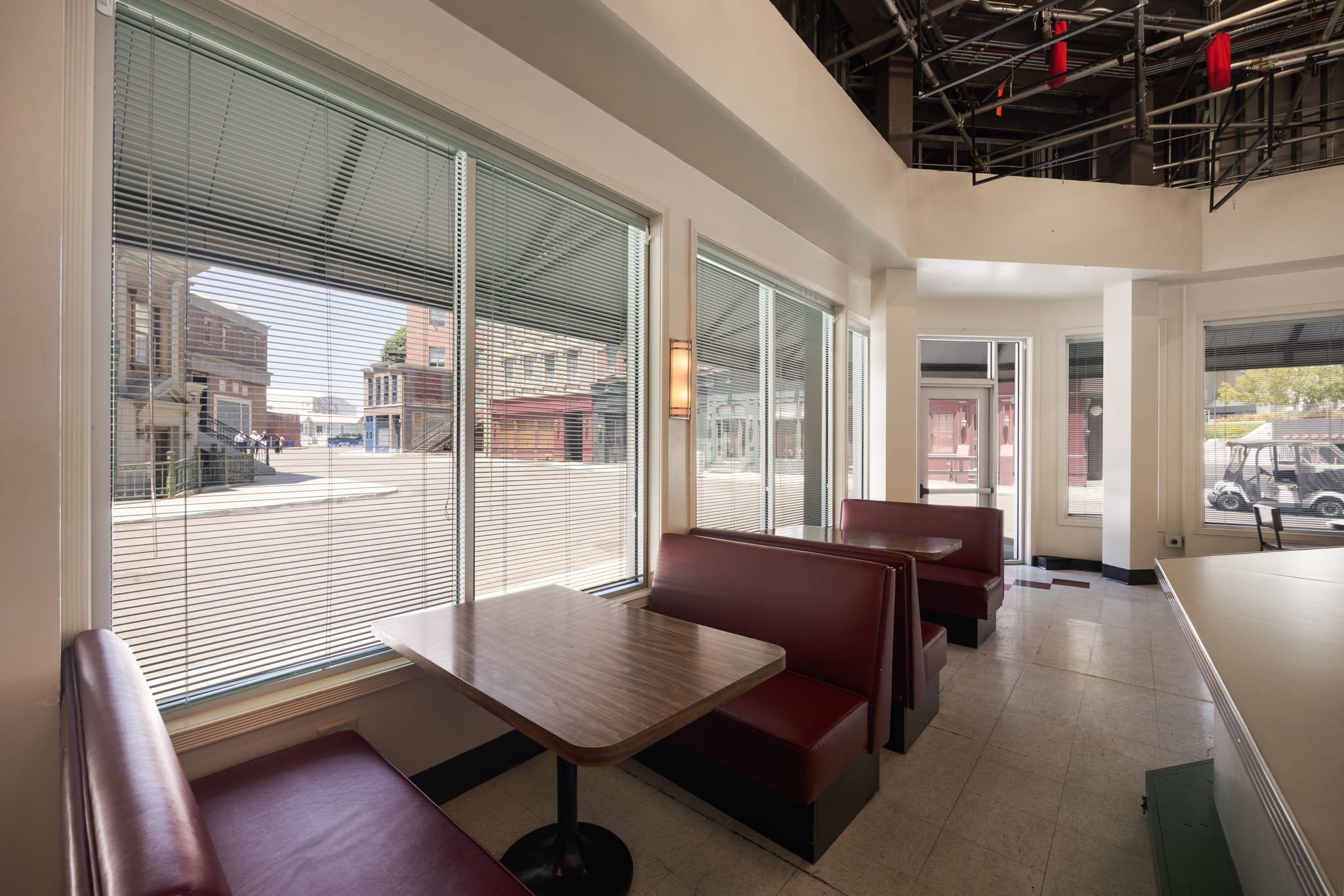 Diner interior with red booths, a street facade visible through windows, and exposed film set rigging overhead.