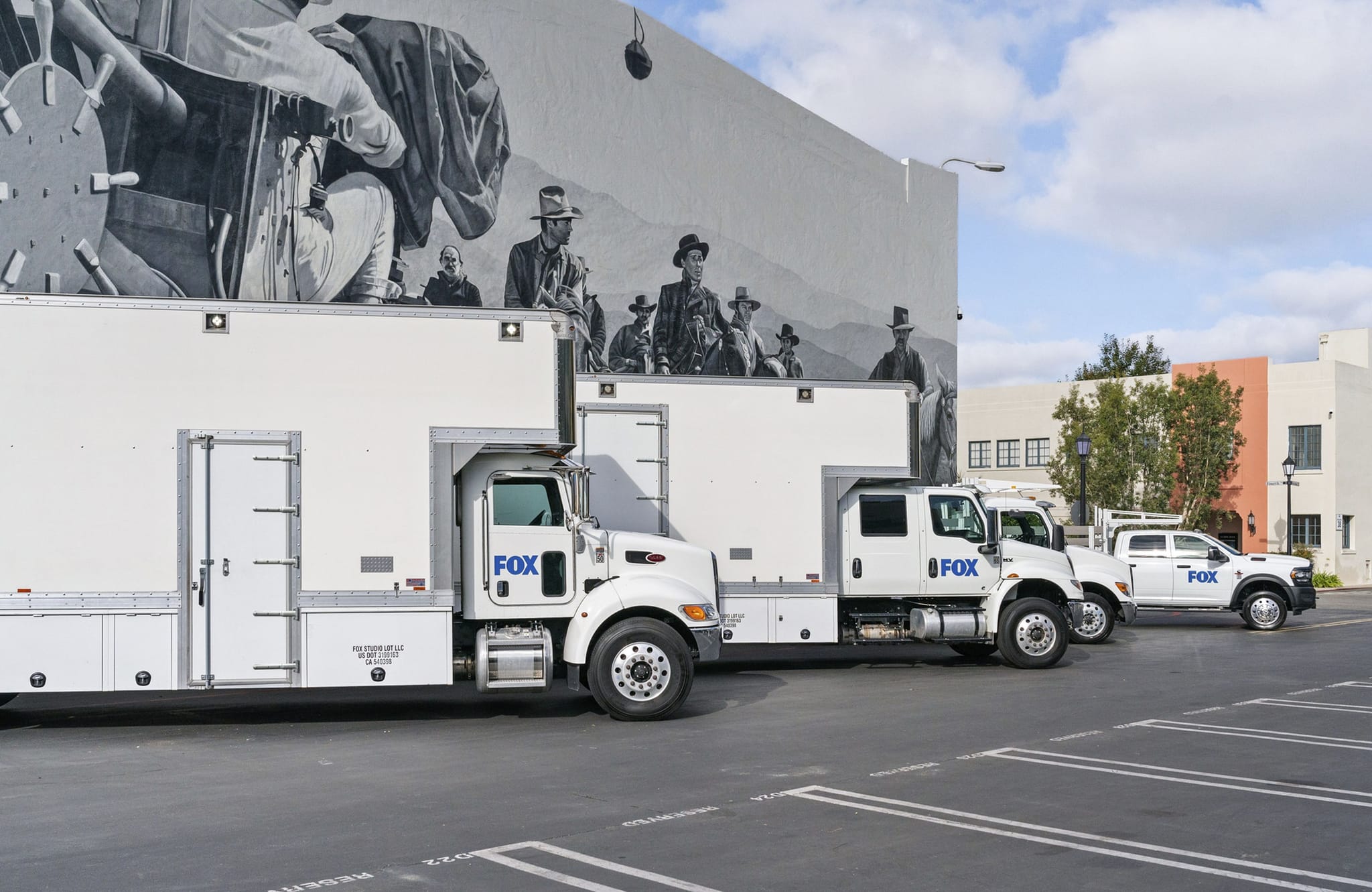 White Fox production trucks and a pickup parked by a building with a black and white mural.