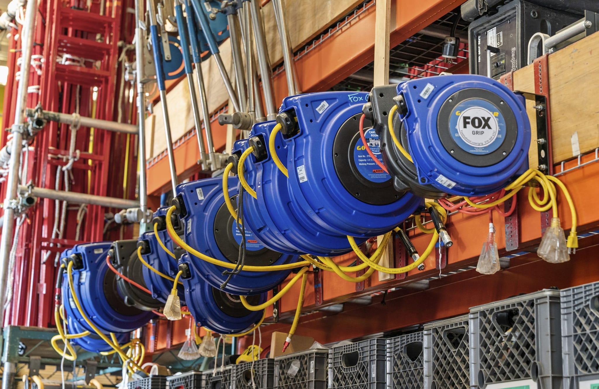A row of blue cable reels with yellow cords mounted on an industrial shelf.