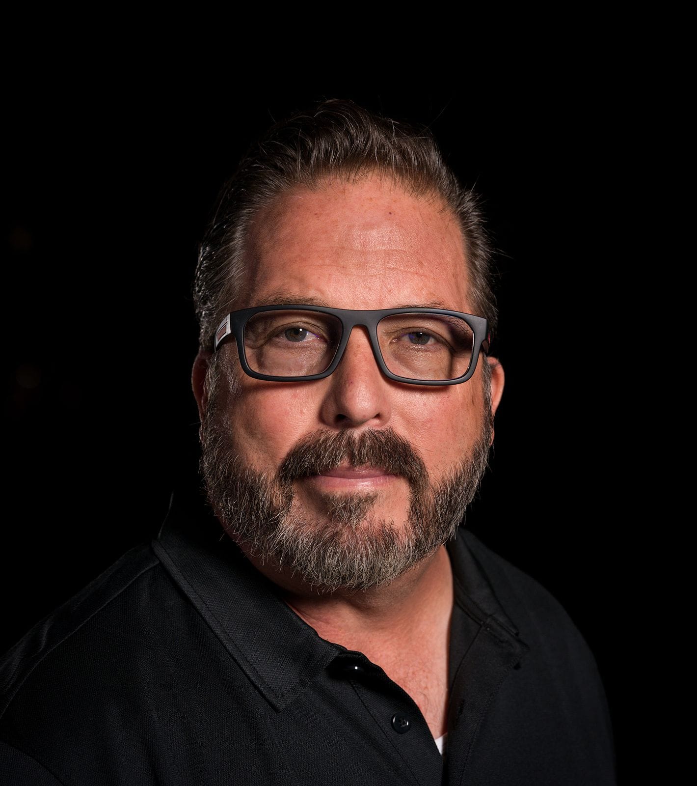 A man with a beard and black-framed glasses looks forward.
