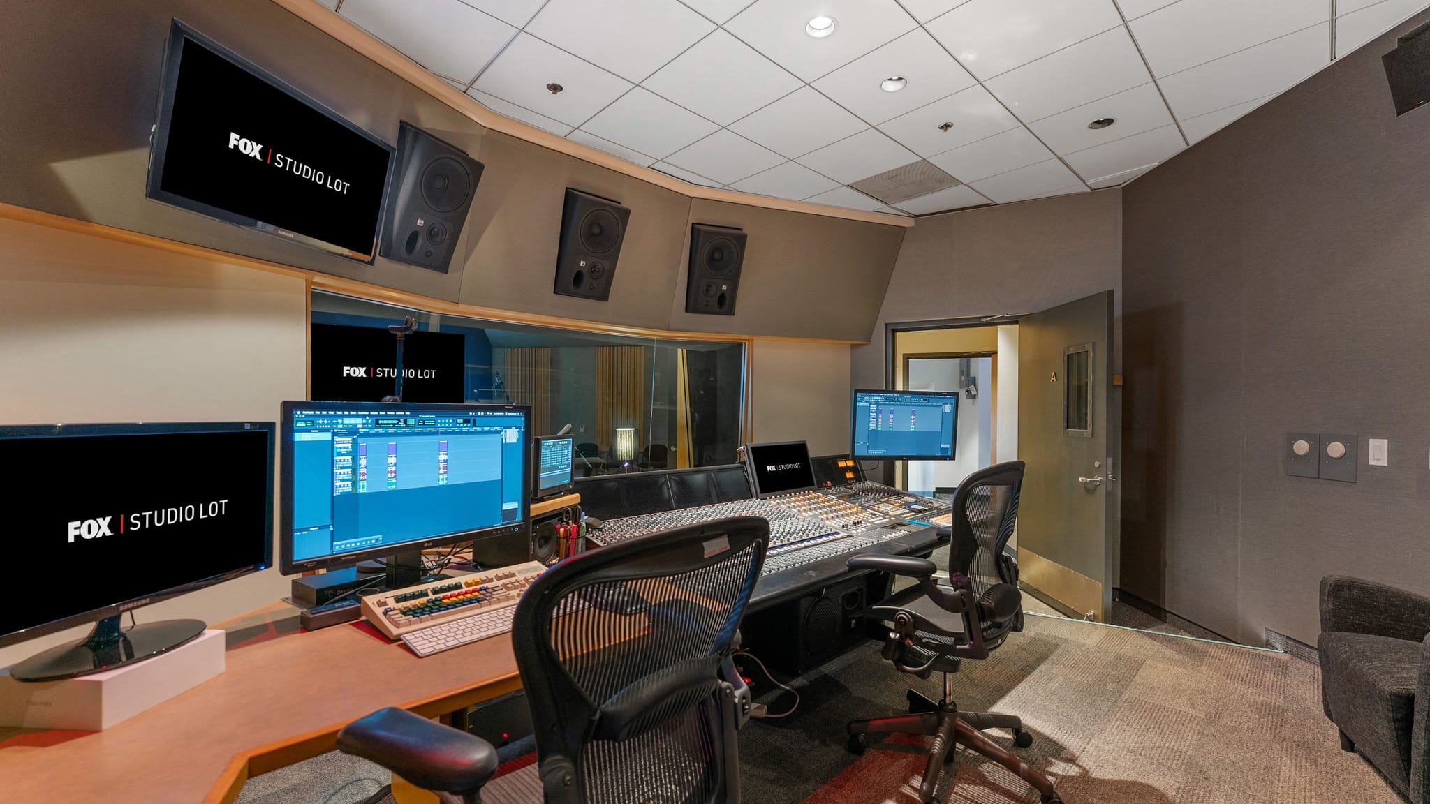 A professional sound mixing studio featuring a large console, multiple computer monitors, and wall-mounted speakers.
