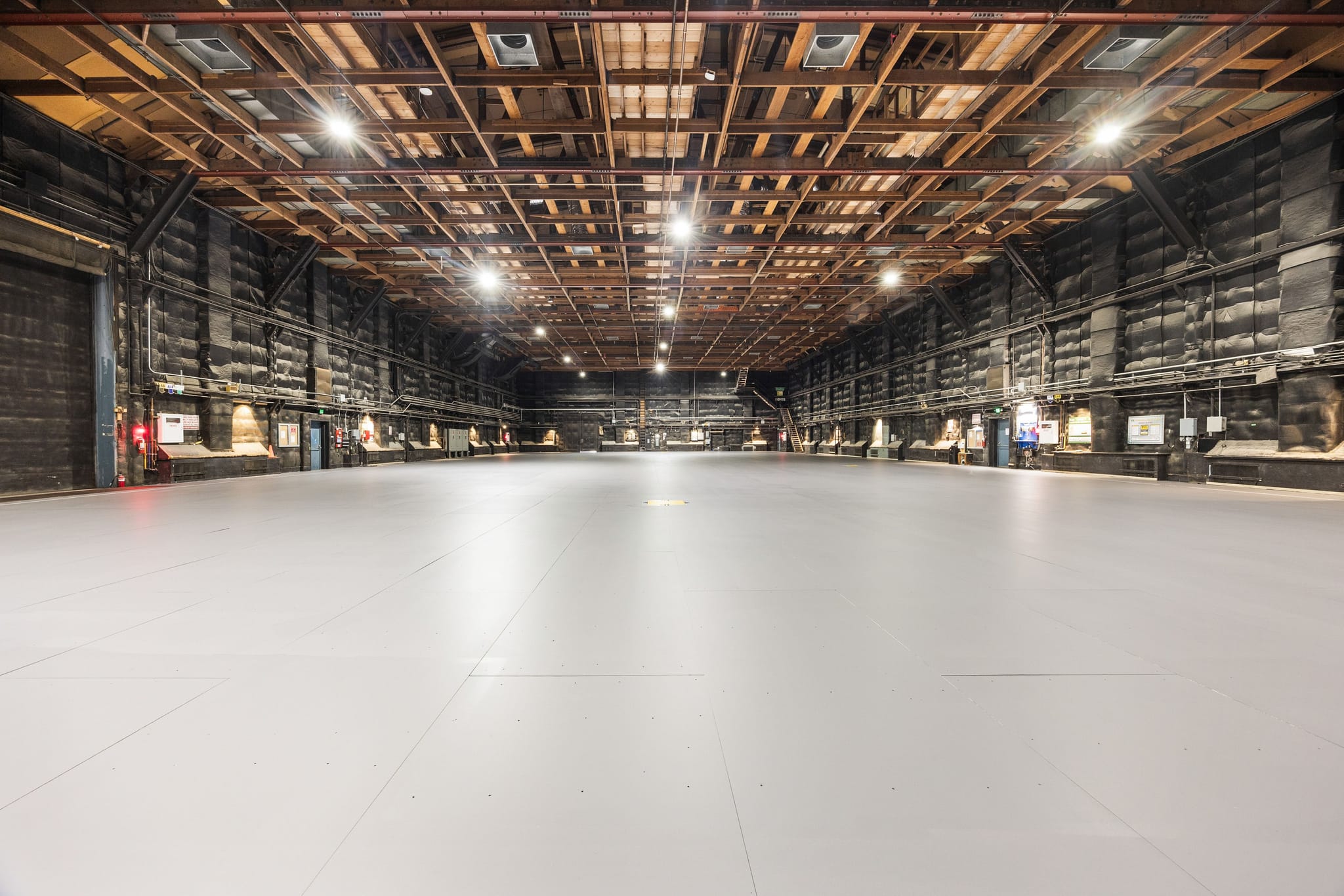 Large, empty soundstage with a light gray floor, dark walls, and an exposed wooden beam ceiling.